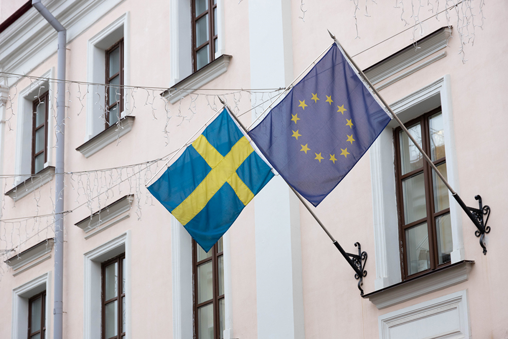 Svenska flaggan och EU-flaggan på en fasad.