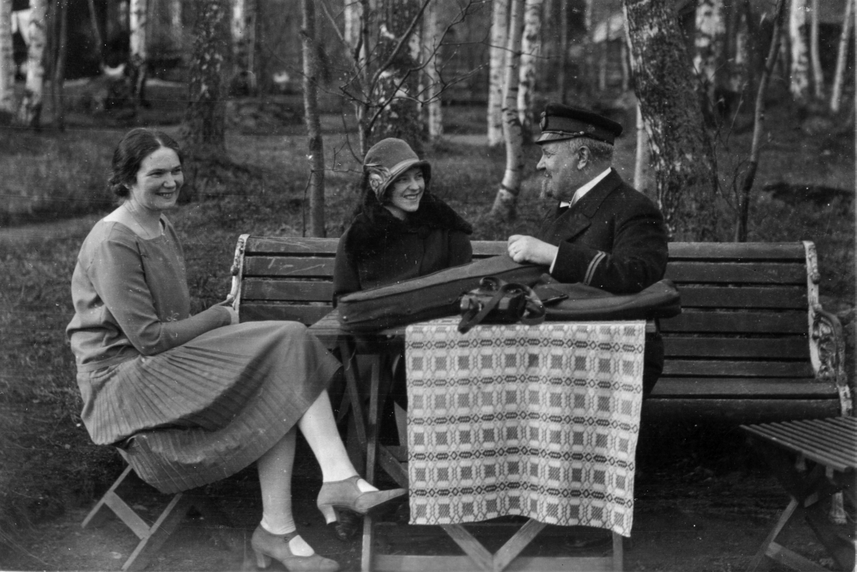 Karl Tirén i tjänsteuniform, sitter på en bänk tillsammans med två kvinnor