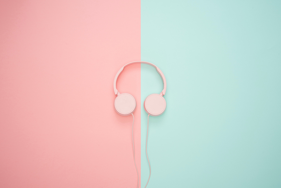 Ett par enkla hörlurar ligger mitt på en bakrund som är till hälften färgad rosa och till hälften färgad mintblå.