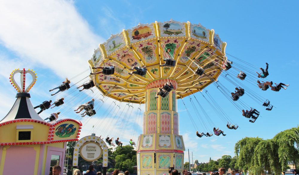 Fotografi föreställande en karusell med gungor, fullsatt och med massvis av människor runt omkring, en sommardag på nöjesparken Gröna lund.