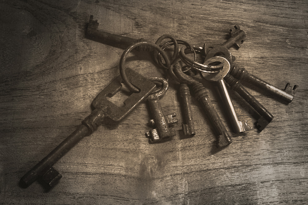 Ett knippe stora, äldre nycklar ligger på ett rustikt träbord.