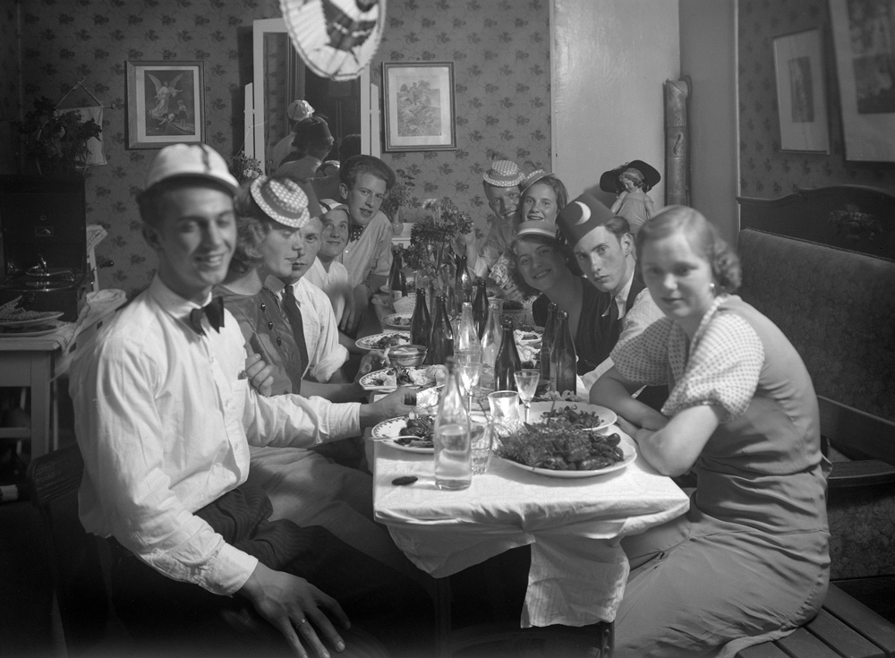 svartvitt fotografi med människor runt ett uppdukat bord, i bakgrunden hänger en kräftlykta