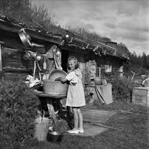 Flicka står vid utomhusbord och diskar. 
