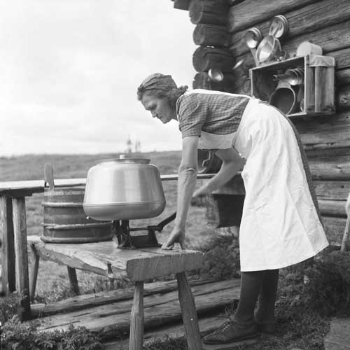 Kvinna utomhus vevar på smörkärna i metall. 