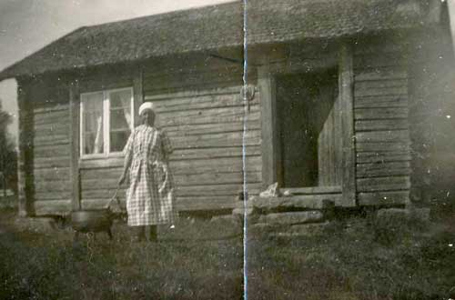 Kvinna står bredvid en trefotad gryta utanför ett hus. 
