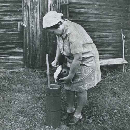 Kvinna häller massa från en kanna ner i en smörkärna av trä.