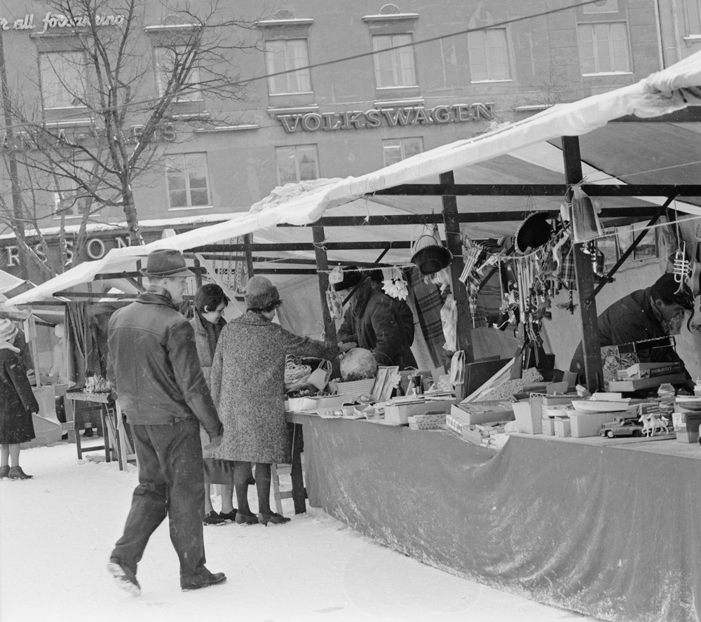 svartvitt fotografi med vinterklädda människor som vandrar mellan marknadsstånd.