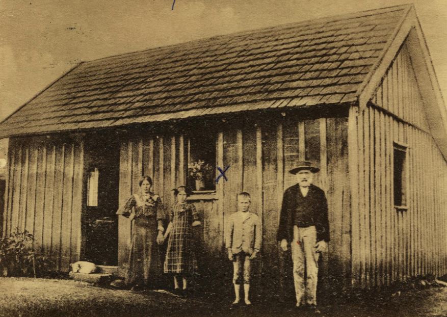 Svartvitt fotografi med familj uppställd framför ett hus.