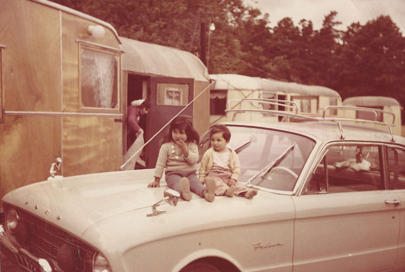 två små barn som sitter på ett biltak med husvagnar i nakgrunden.