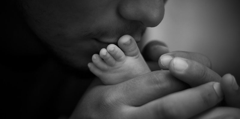 En svartvit bild på en vuxen som böjer sig fram och pussar en babyfot.