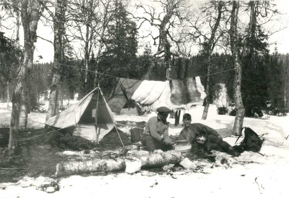 Två män vilar på marken utanför ett tält.