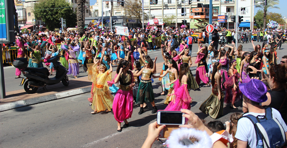karnevalståg i stadsmiljö med utklädda ungdomar som dansar och publik som tittar på