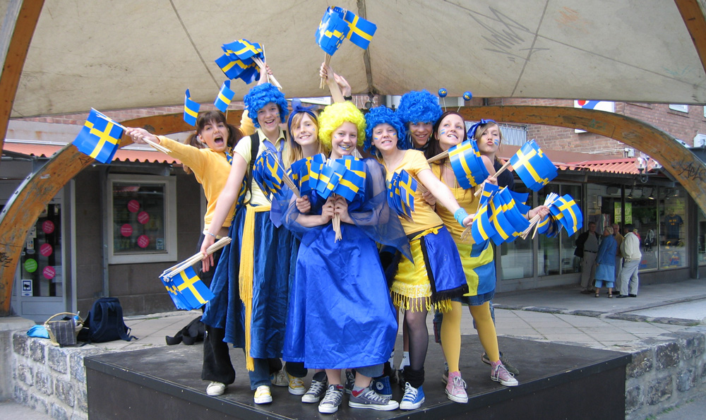 grupp ungdomar klädda i blått och gult som står på en liten scen och viftar med flaggor