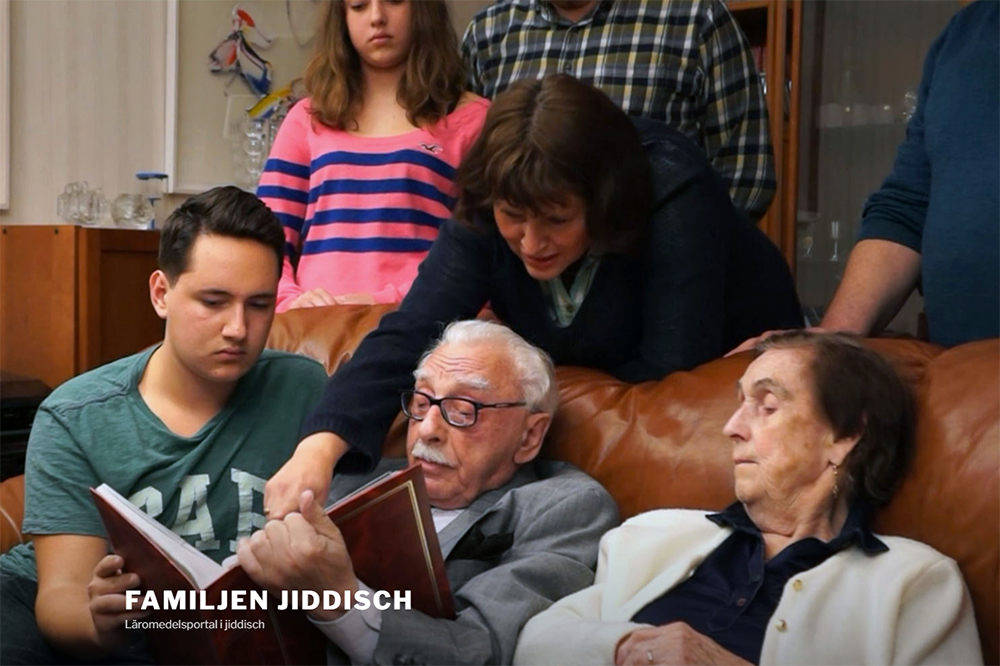 En familj av flera generationer sitter i en soffa och läser en bok.