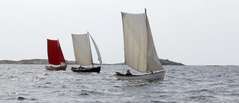 Tre segelförsedda träbåtar som seglar på blått vatten.