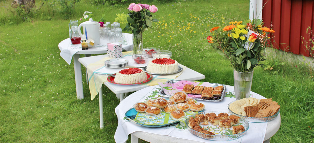 Foto på bord med tårtor, kakor och blommor.