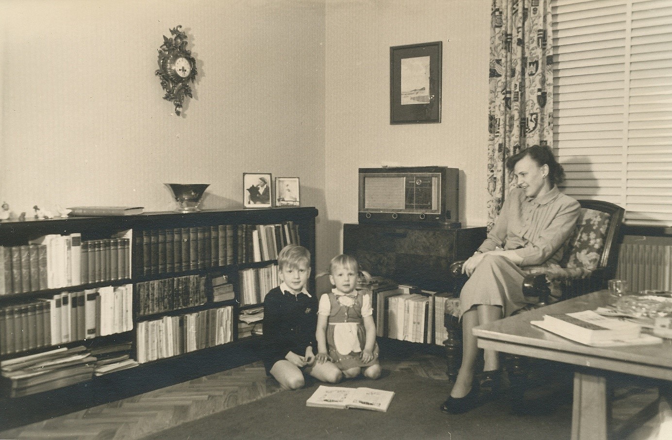 Kvinna och två barn fotograferade i rum med radio i bakgrunden.
