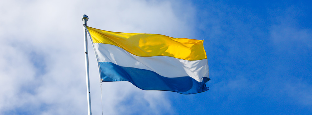 Tornedalingarnas flagga med tre horisontella fält i gult, vitt och blått som vajar i vinden.