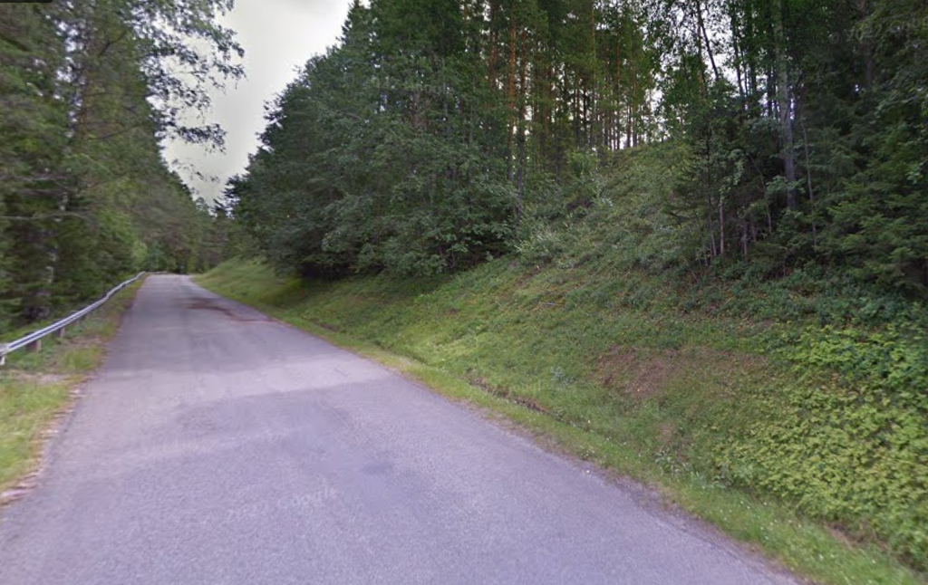 På ett foto ser man landsväg 968 i riktning mot byn Åsmon ovanför Tjekesmyran/Tjekesbäcksmyran. Man ser att vägen går uppför genom nipan/sluttningen och man ser delar av den branta nipan tydligt till höger om vägen.