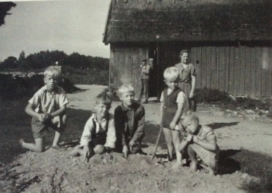 Svartvitt fotografi med fem barn som sitter på knä i grushög. 