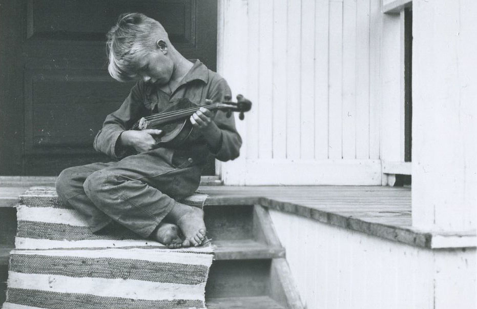 Pojke sitter på farstutrapp med fiol i famnen.