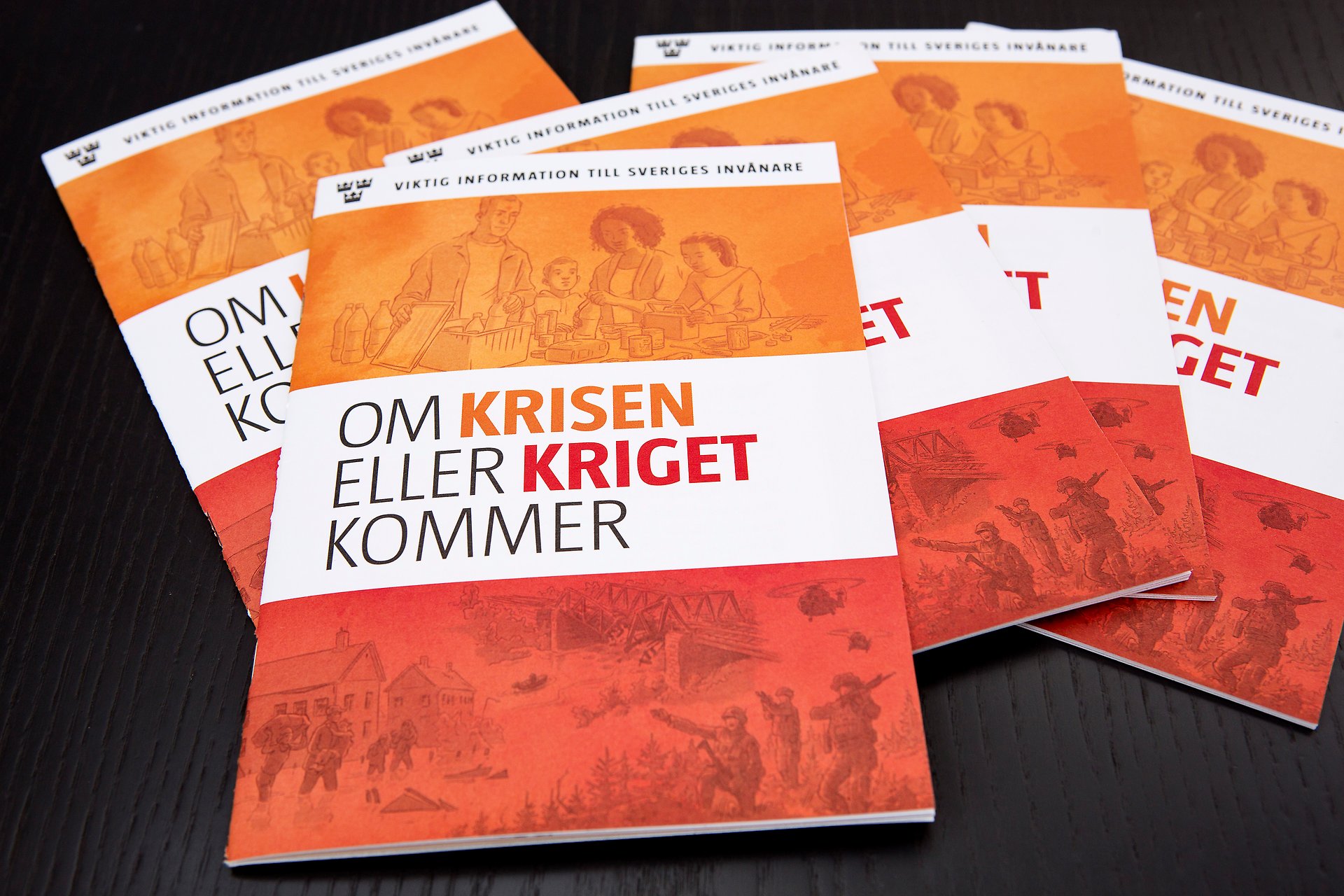 En hög med broschyrer som ligger på en svart bakgrund. Broschyren är i orange och rött och har titeln "Om krisen eller kriget kommer".