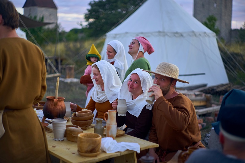 Kvinnor och män i medeltida kläder äter och dricker.