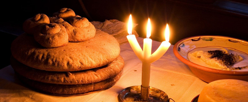 Foto på ett bord dukat med gröt, bröd och ett trearmat ljus.