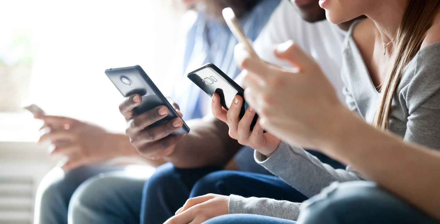 Närbild på ungdomar som sitter med mobiltelefoner.