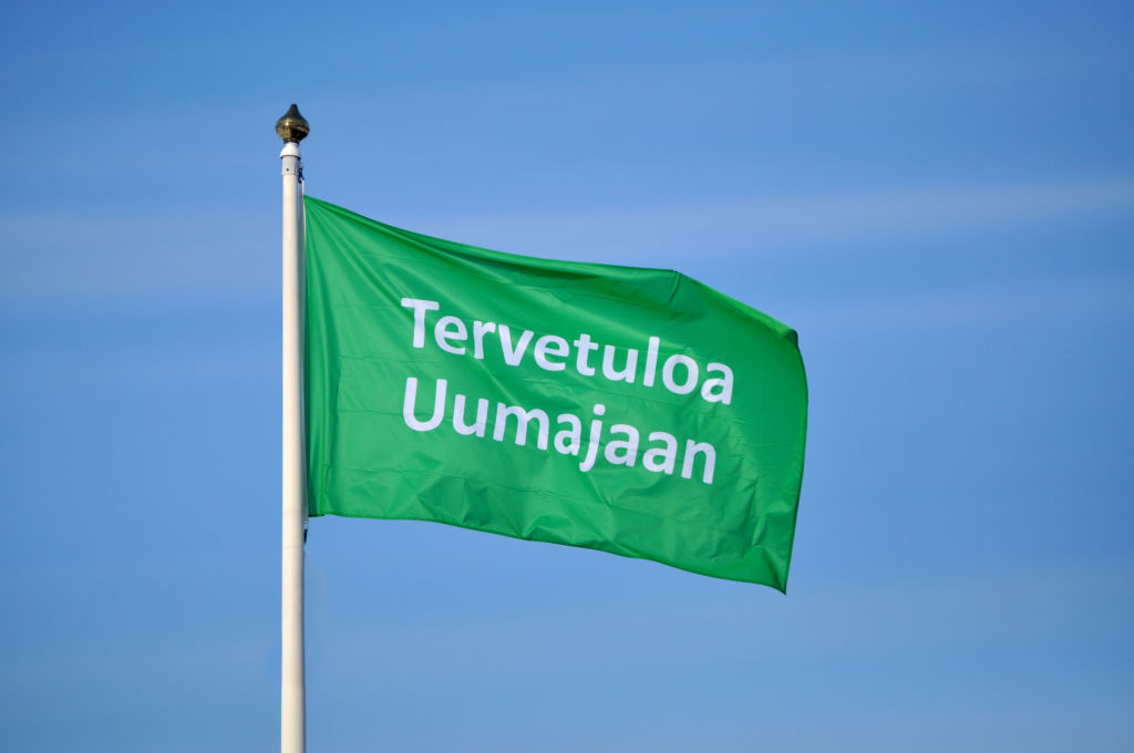 Hissad grön flagga med vit text på finska: "Tervetuloa Uumajaan" (Välkommen till Umeå).