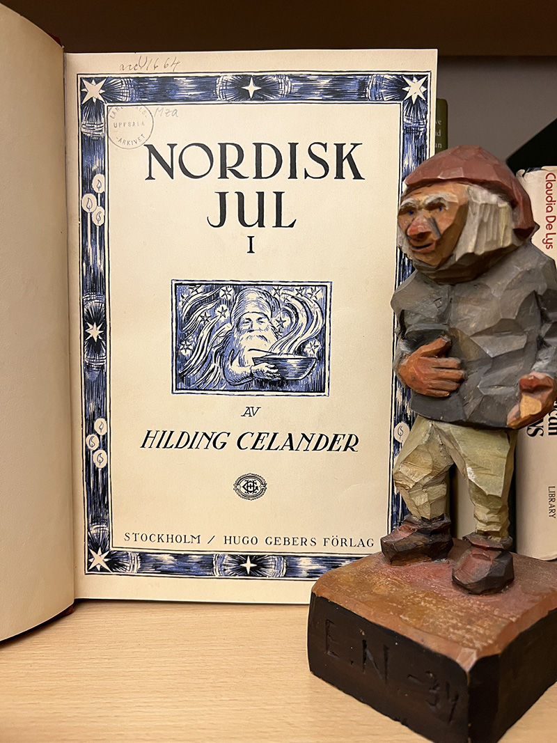 Första uppslaget av en bok där det står Nordisk jul 1 av Hilding Celander. Bredvid boken står en snidad tomte.