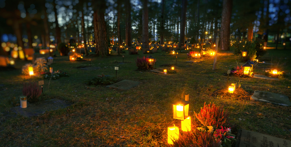 bild från kyrkogård i skymning där det brinner ljus på nästan alla gravar