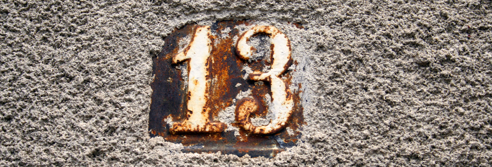 rostig nummerskylt med siffran 13 på betongvägg