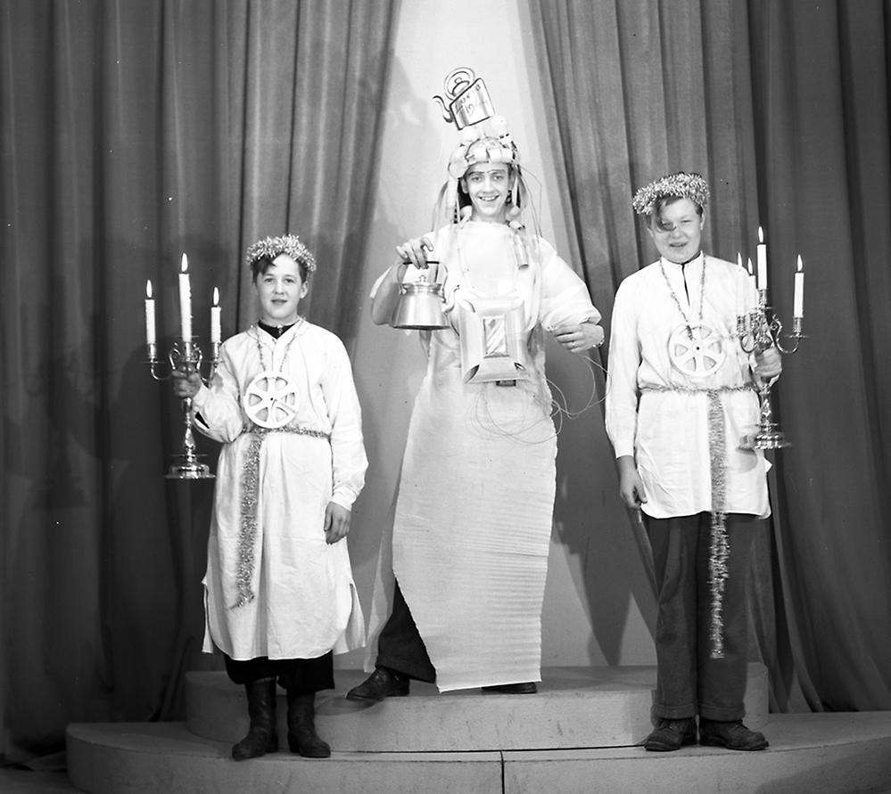 svartvitt fotografi med tre ungdomar utklädda för luciafirande - lucia i mitten med en kaffekanna på huvudet