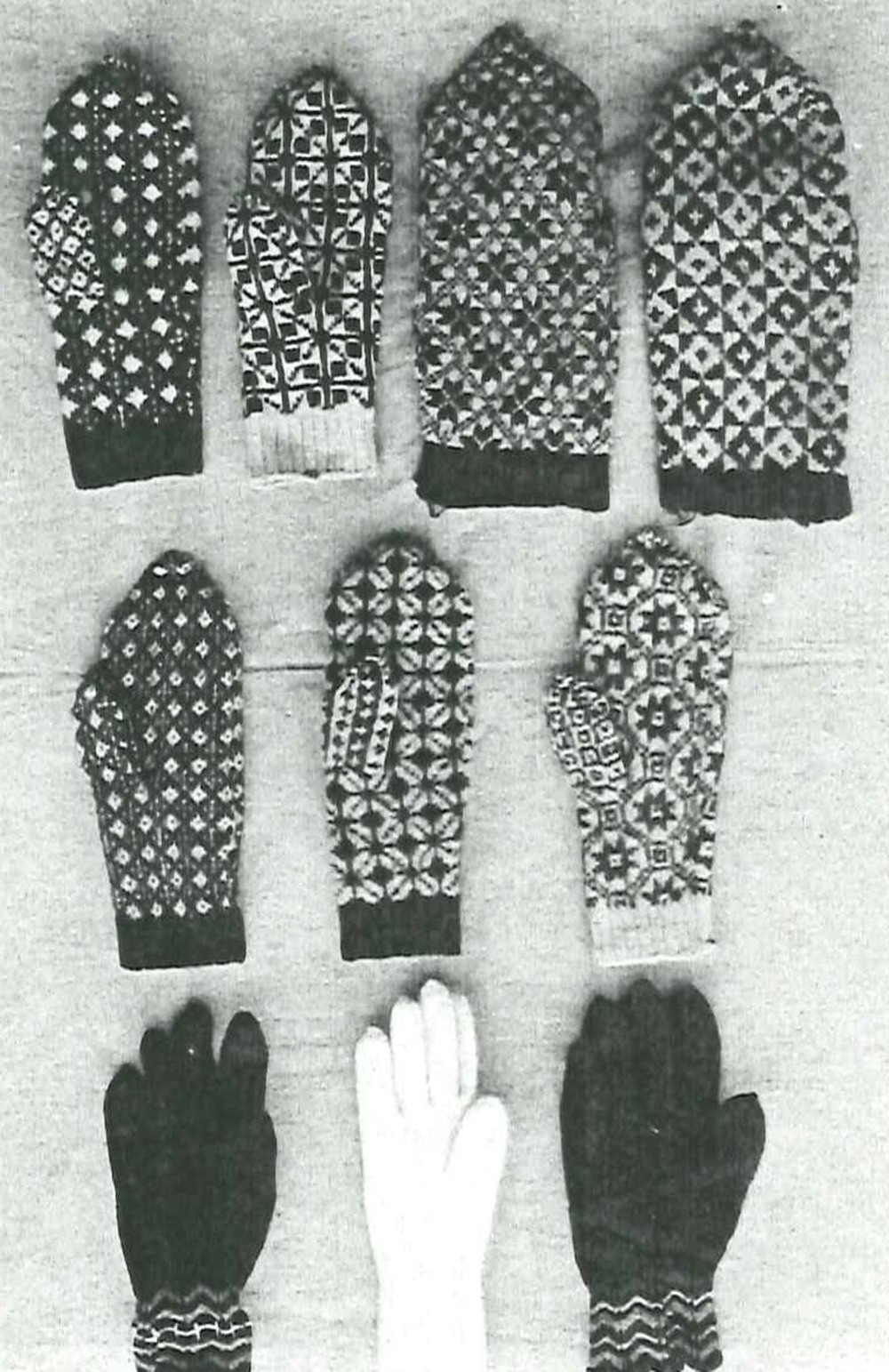 Svartvitt foto av tio stycken vantar lagda i tre rader. Sju av vantarna är mönsterstickade tumvantar i två färger, tre är enfärgade fingervantar. 
