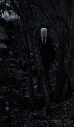svartvitt fotografi med otydlig kostymklädd gestalt en bit in i skogen.